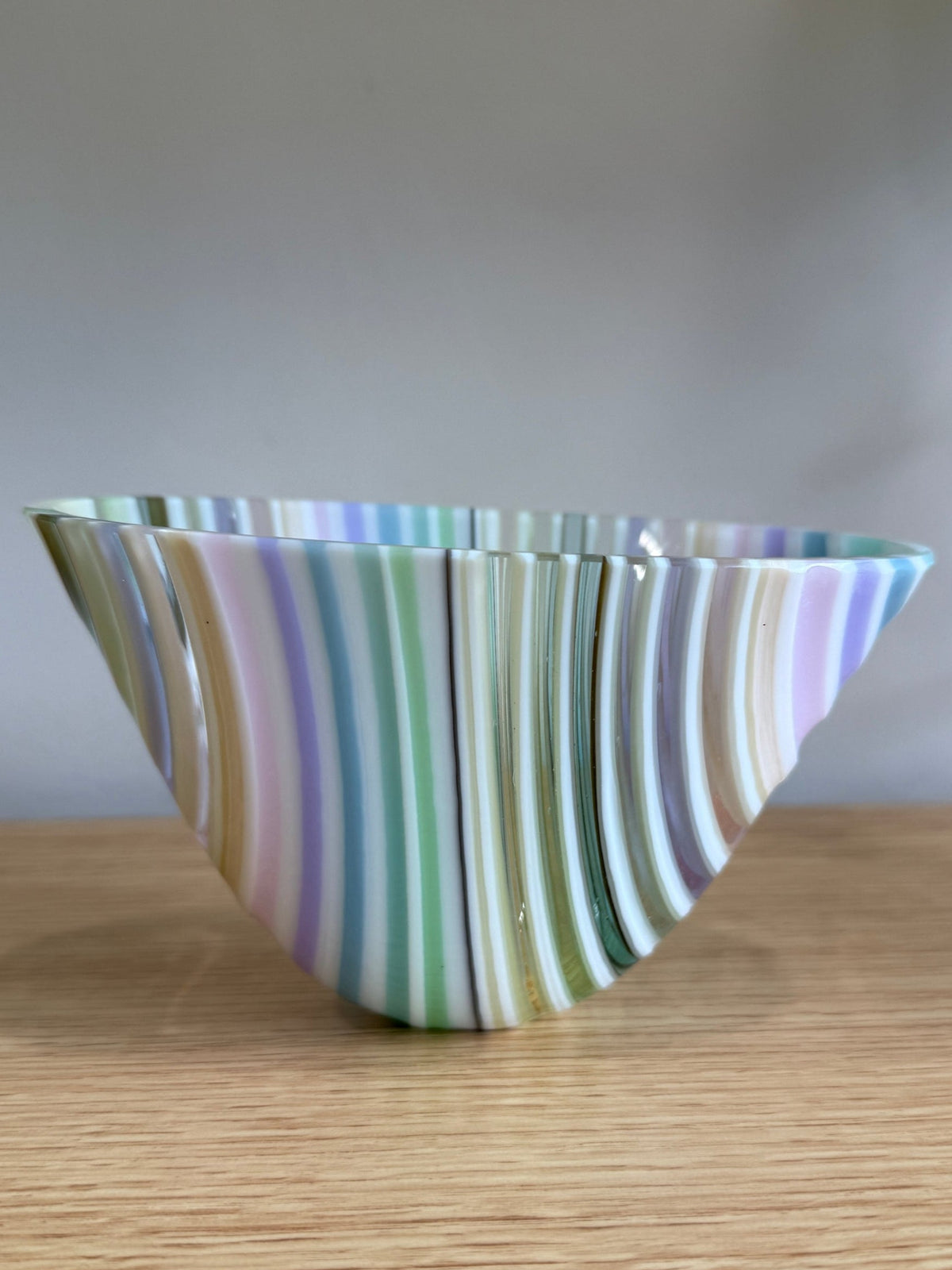 Pastel Rainbow Striped glass bowl on a wooden surface with a neutral background