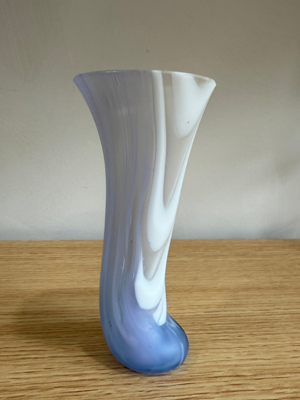 White and blue glass vase on a wooden surface with a plain background