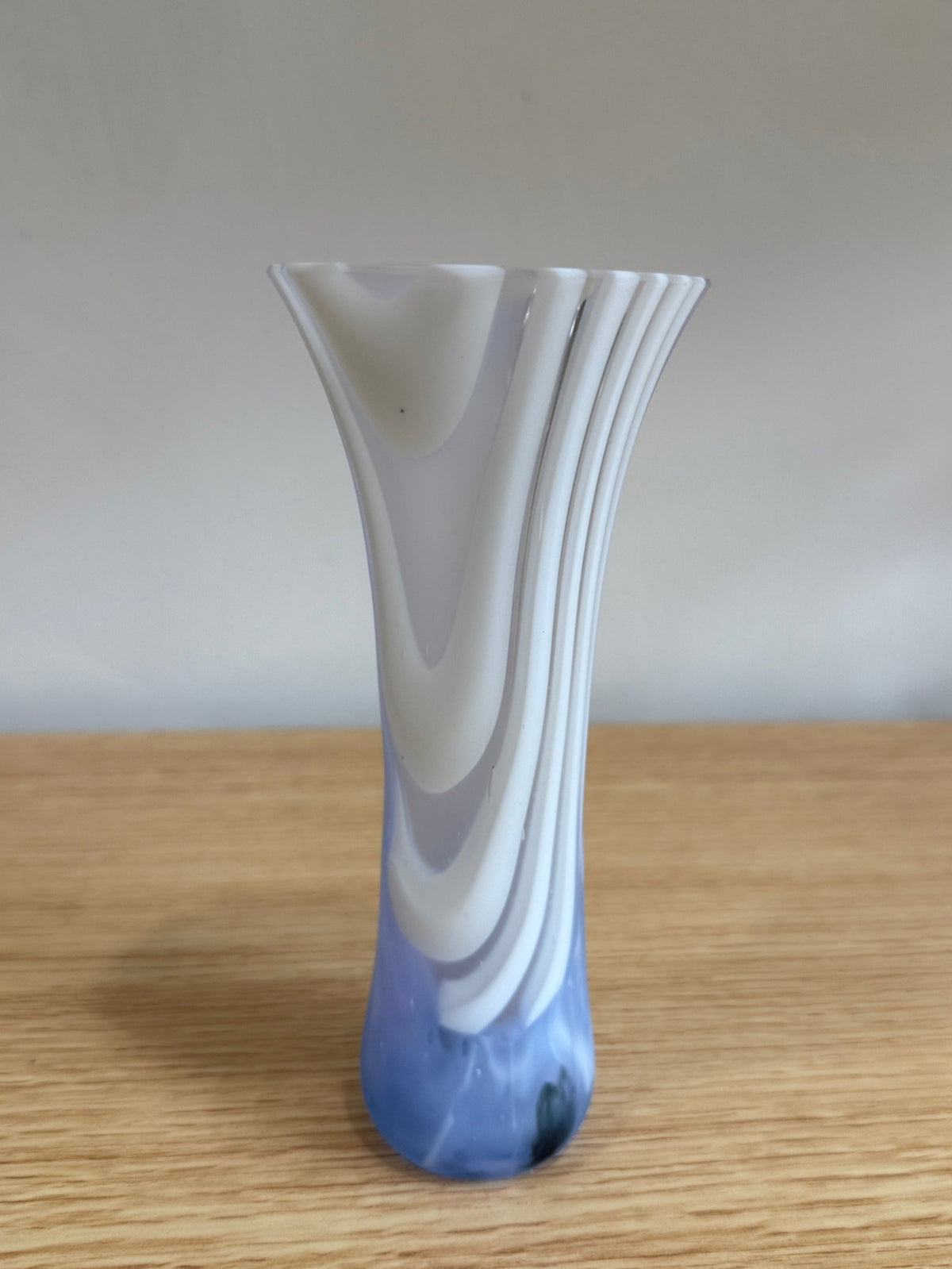 White and blue glass vase on a wooden surface with a plain background