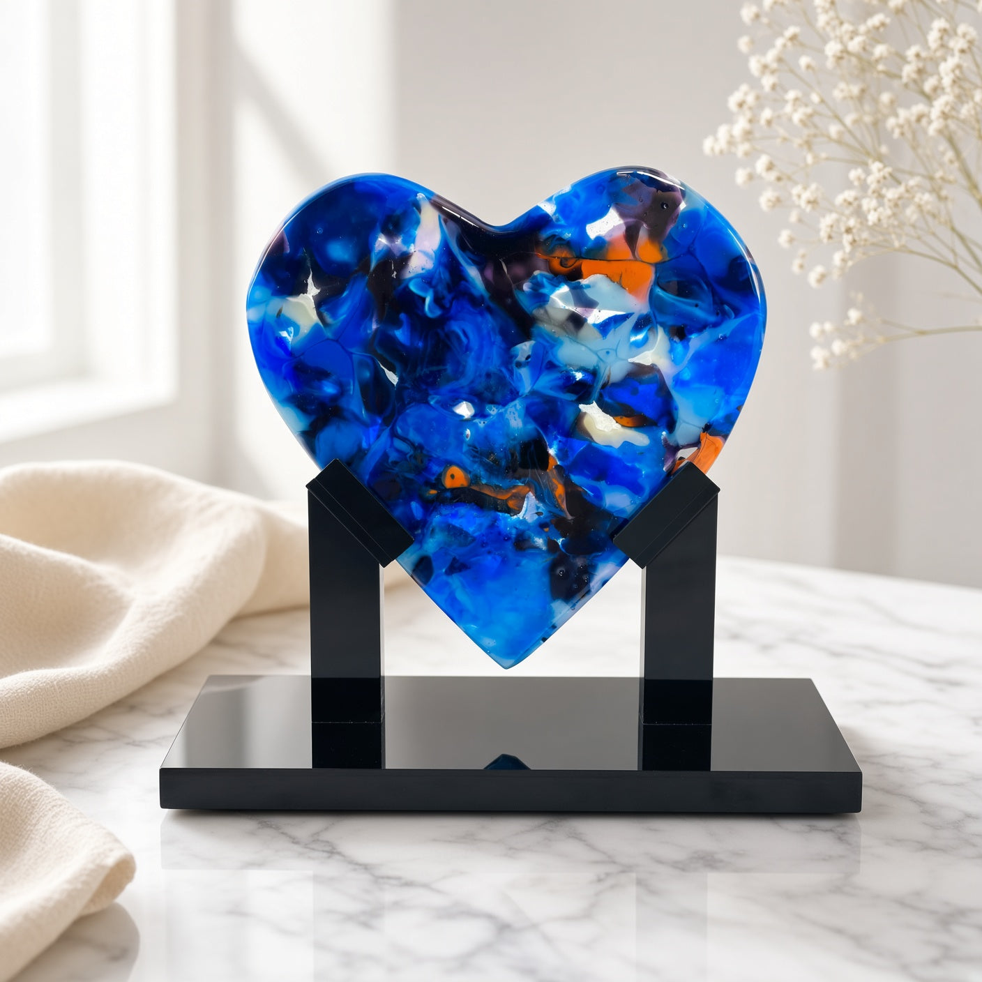 Navy blue and orange fused glass heart sculpture on black stand, staged on a marble surface with dried flowers - handmade art glass gift