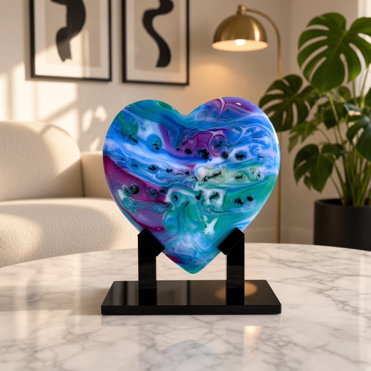 Blue, purple, and teal marbled glass heart sculpture on a black stand, displayed on a marble table in a modern living room - handmade fused art glass keepsake