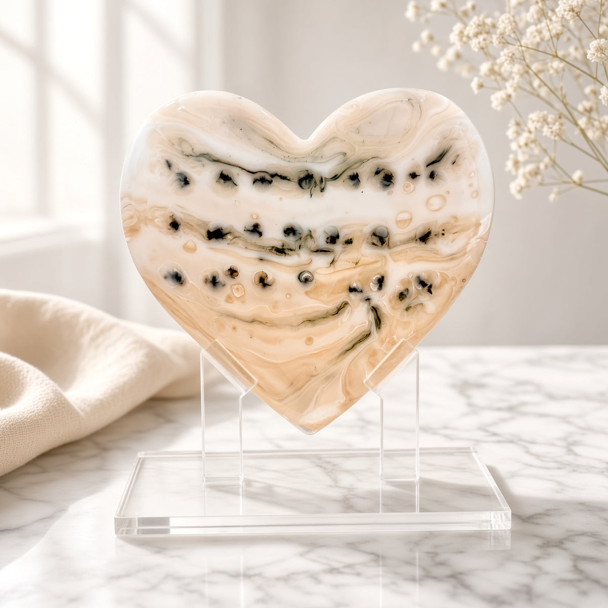 Neutral cream and black speckled glass heart sculpture on a clear acrylic stand on a marble surface - handmade fused art glass keepsake