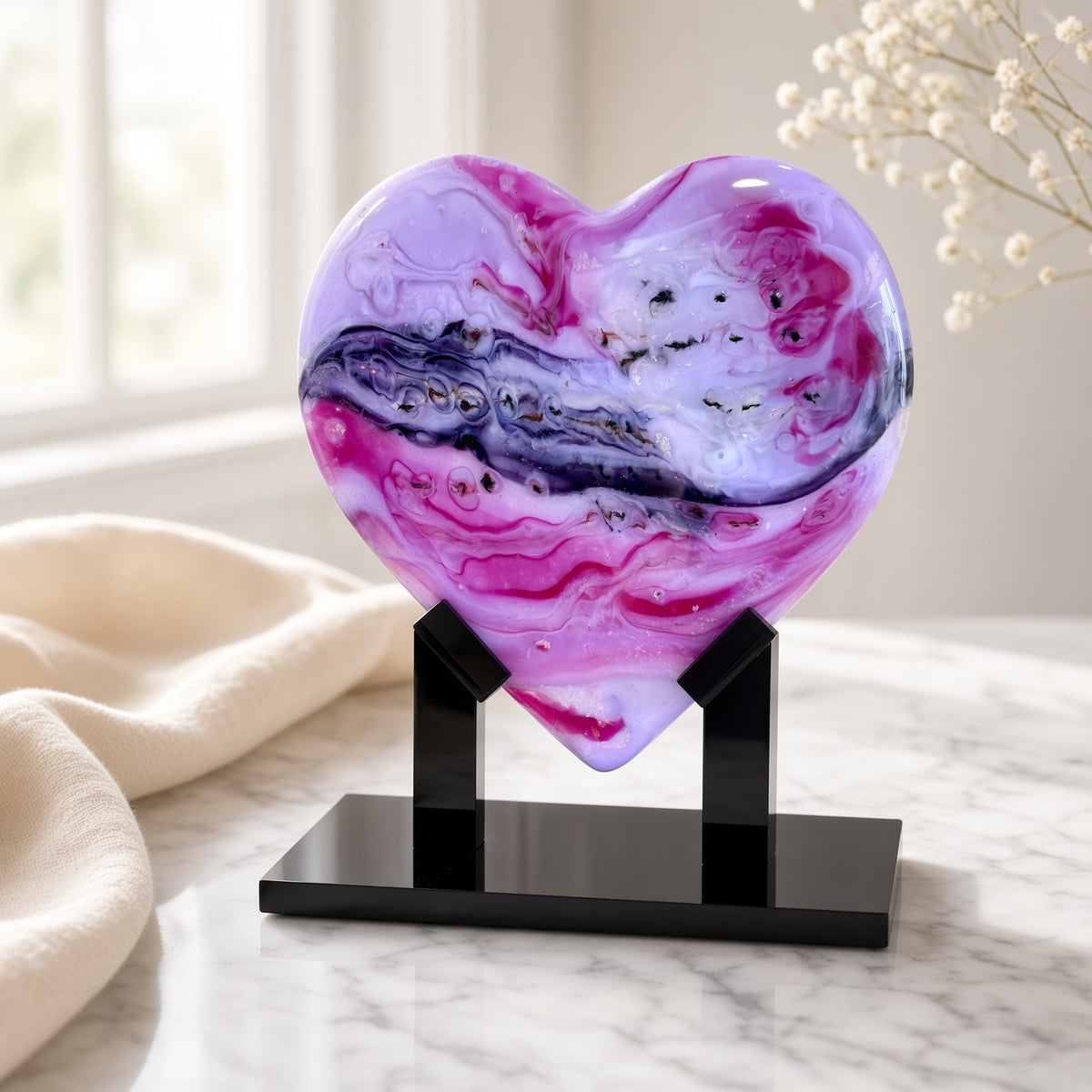 Purple, pink, and white marbled glass heart sculpture on a black stand on a marble surface - handmade fused art glass keepsake
