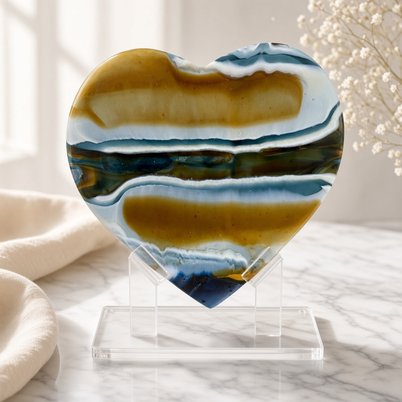 Amber and navy blue banded fused glass heart sculpture on clear acrylic stand, styled on marble surface - handmade art glass keepsake