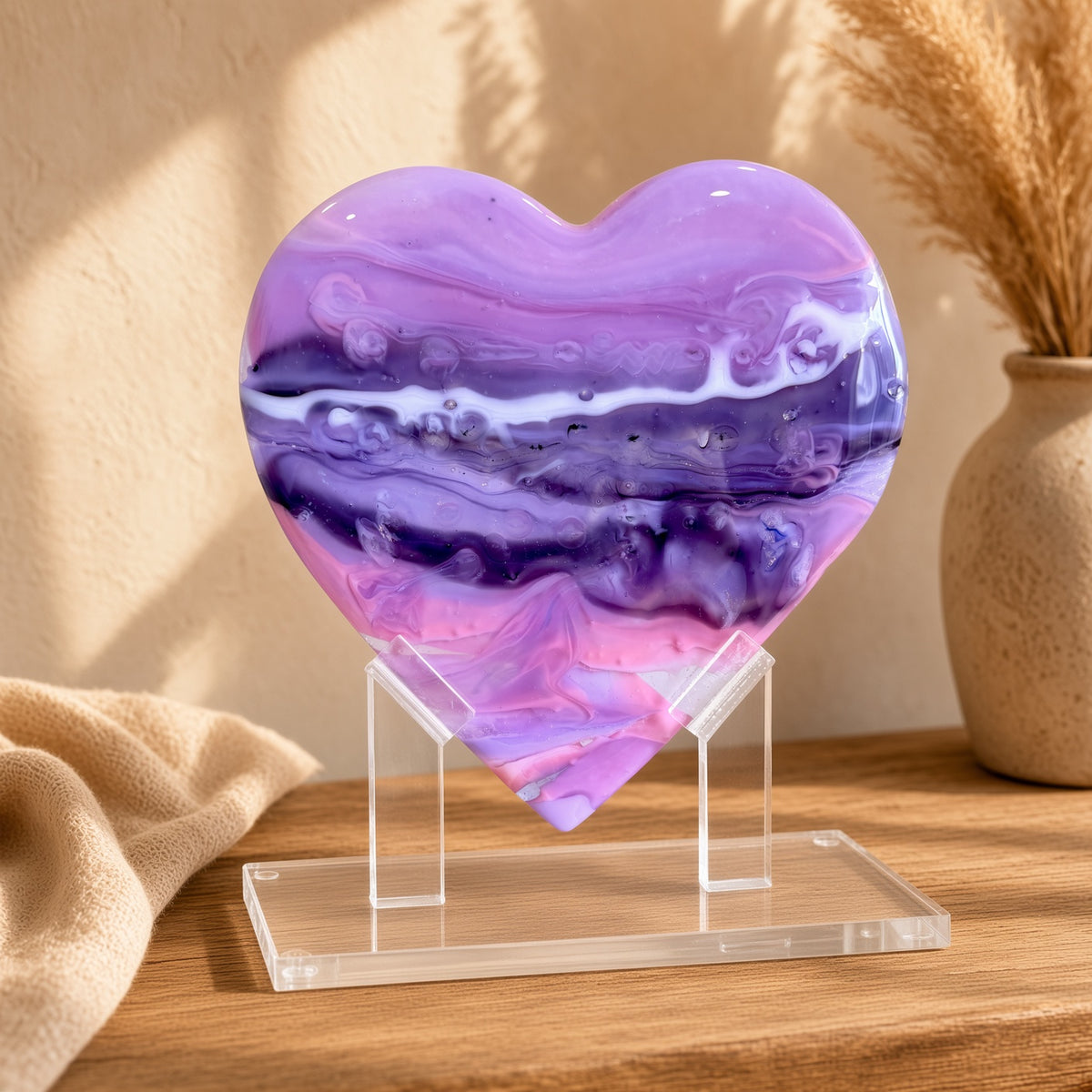 Purple, pink, and white marbled glass heart sculpture on a clear acrylic stand on a wooden table - handmade fused art glass keepsake