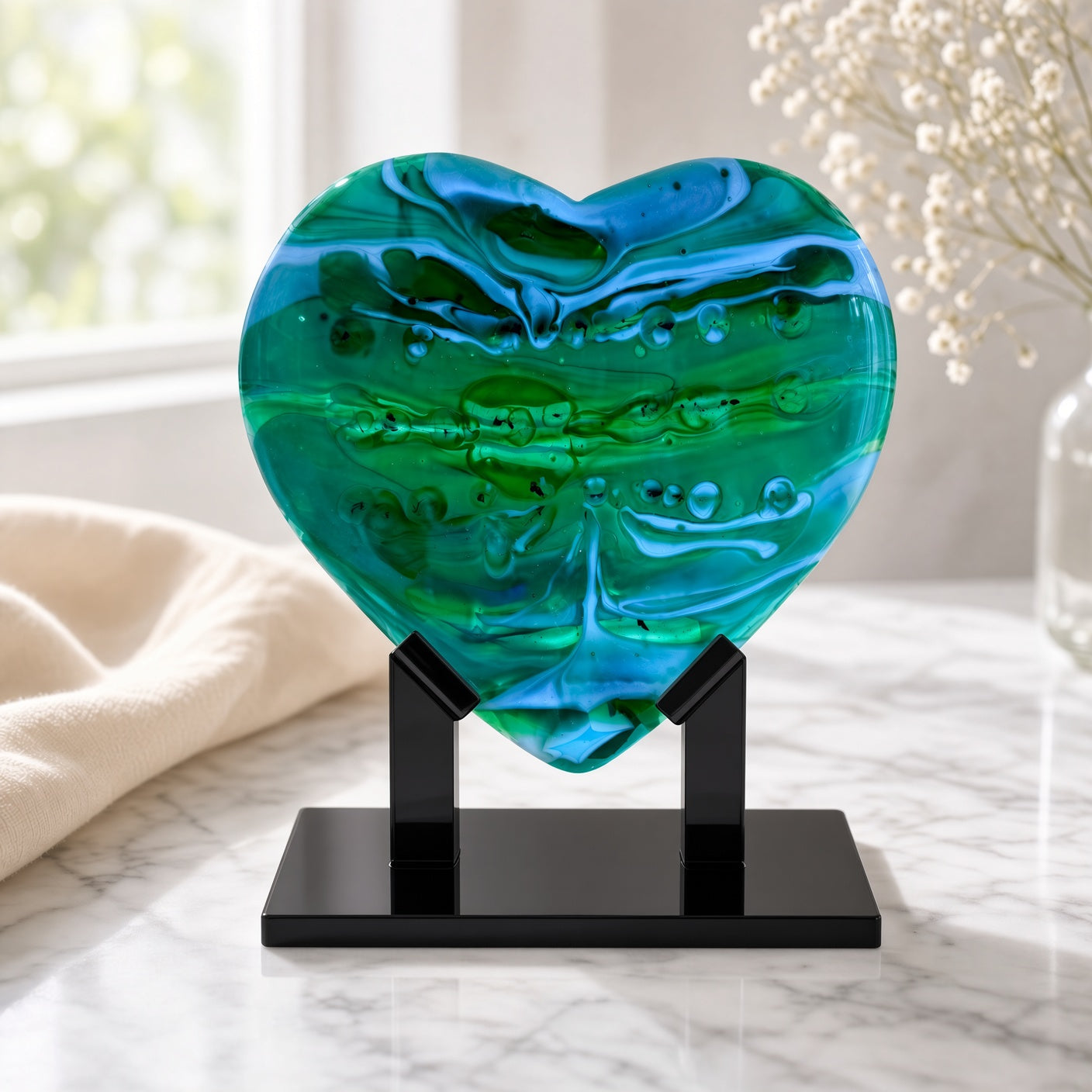 Emerald Tide green fused glass heart sculpture on a black stand, styled on a marble surface with soft linen — handmade art glass decor.
