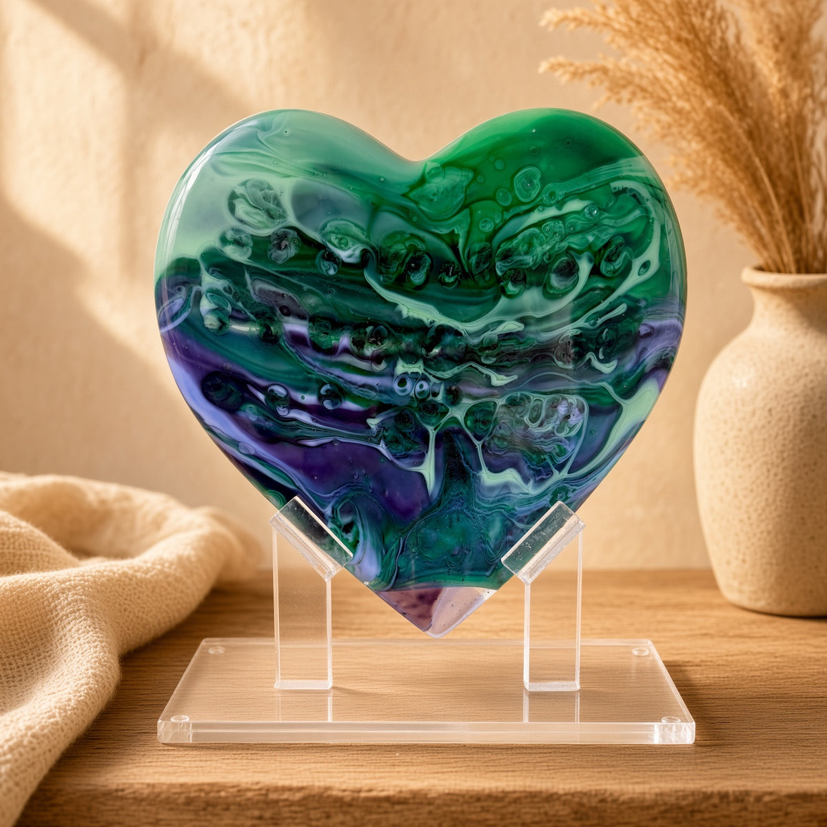 Green, teal, and purple marbled glass heart sculpture on a clear acrylic stand on a wooden table - handmade fused art glass keepsake
