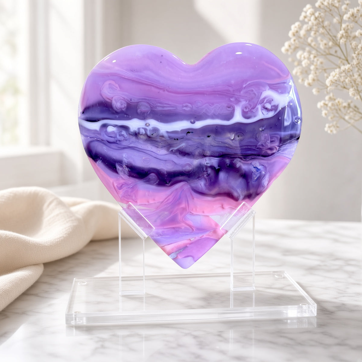Purple, pink, and white marbled glass heart sculpture on a clear acrylic stand on a marble surface - handmade fused art glass keepsake